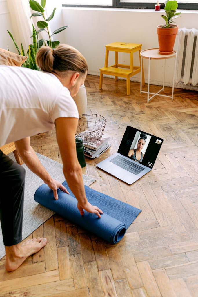 Person setting up a yoga mat for a virtual fitness class at home.
