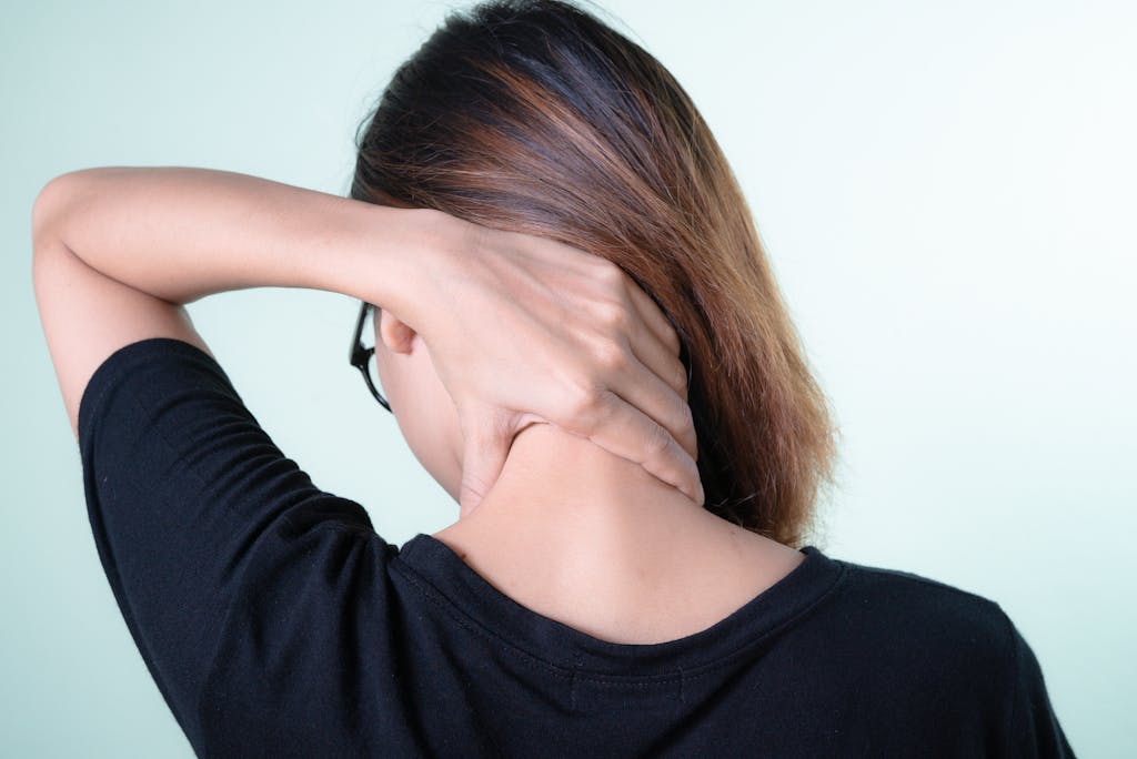 Rear view of a woman massaging her neck, depicting neck pain relief or self-care concepts.